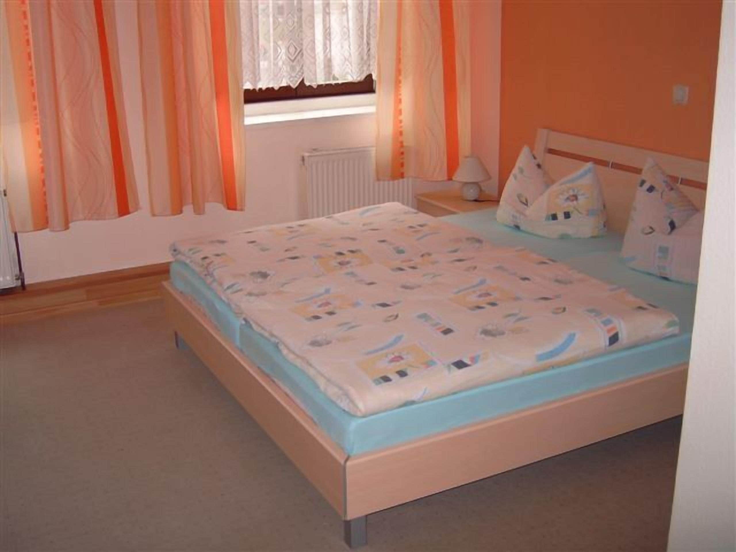 A bedroom with a bed, curtains, a nightstand, and a lamp.