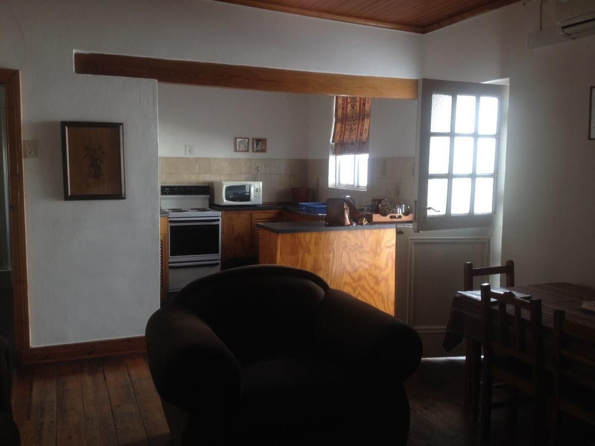 Cocina con microondas, horno y encimera de madera. Hay una silla y una mesa con sillas.
