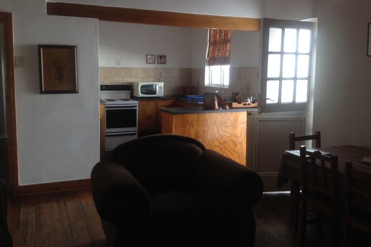 A kitchen with a microwave, oven, and wooden counter. There is a chair and a table with chairs.