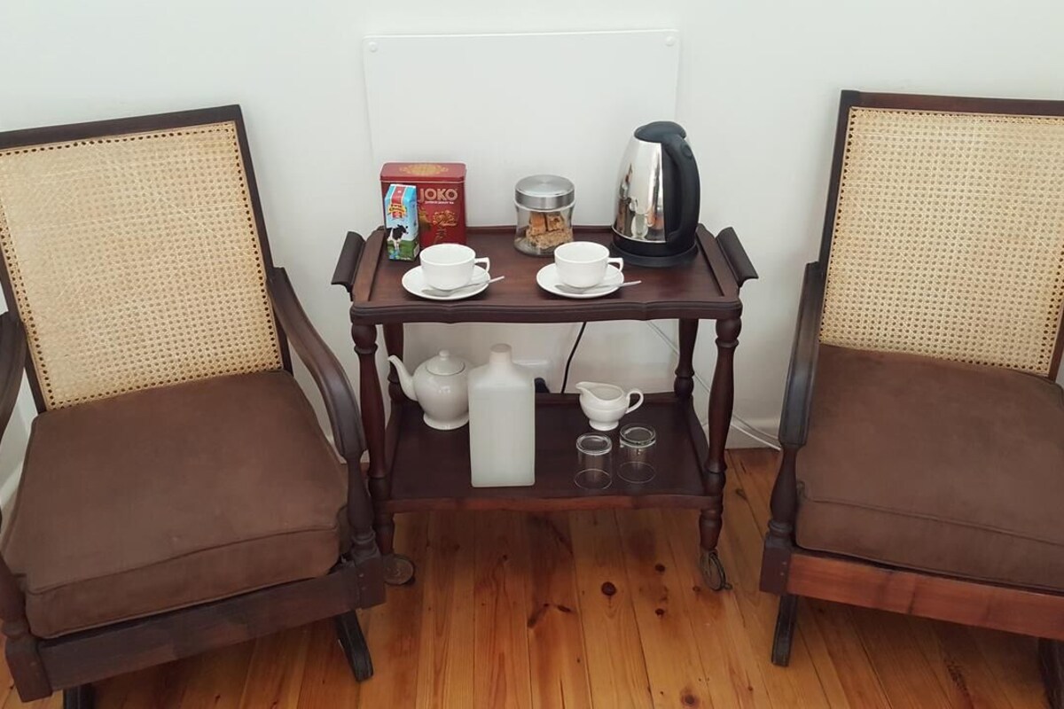 Two brown upholstered chairs with woven backs, a wooden table with a tea set, a box of JOKO tea, and a coffee pot.