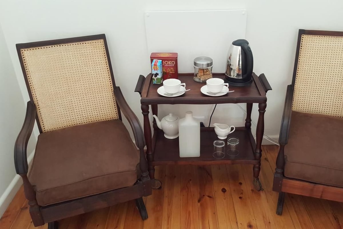 Two brown upholstered chairs with woven backs, a wooden table with a tea set, a box of JOKO tea, and a coffee pot.