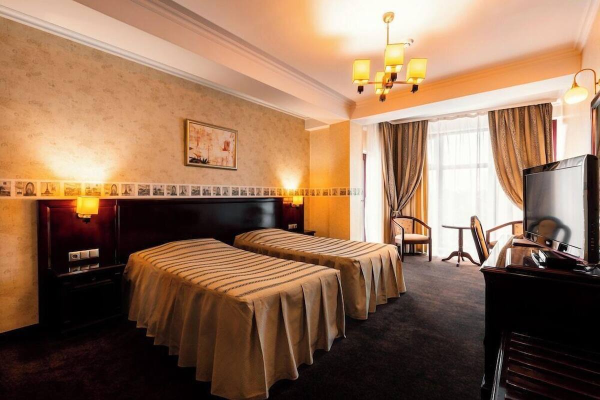 A hotel room with two beds, a desk, a television, and a chandelier.