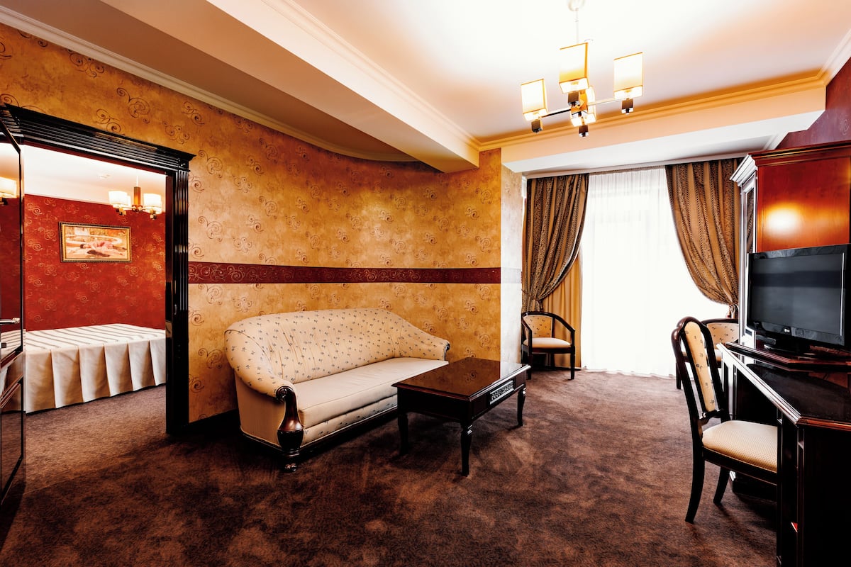 A hotel room with a sofa, a small table, a TV, and a window with curtains.