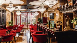 A luxurious bar area with red upholstered chairs, a wooden bar counter, and ornate chandeliers. - President Hotel (Bacioi)