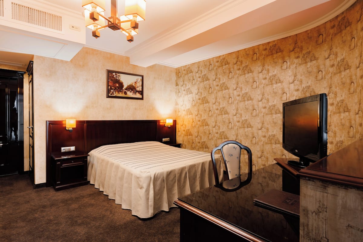 A hotel room with a bed, a desk with a television, a chair, and a nightstand.