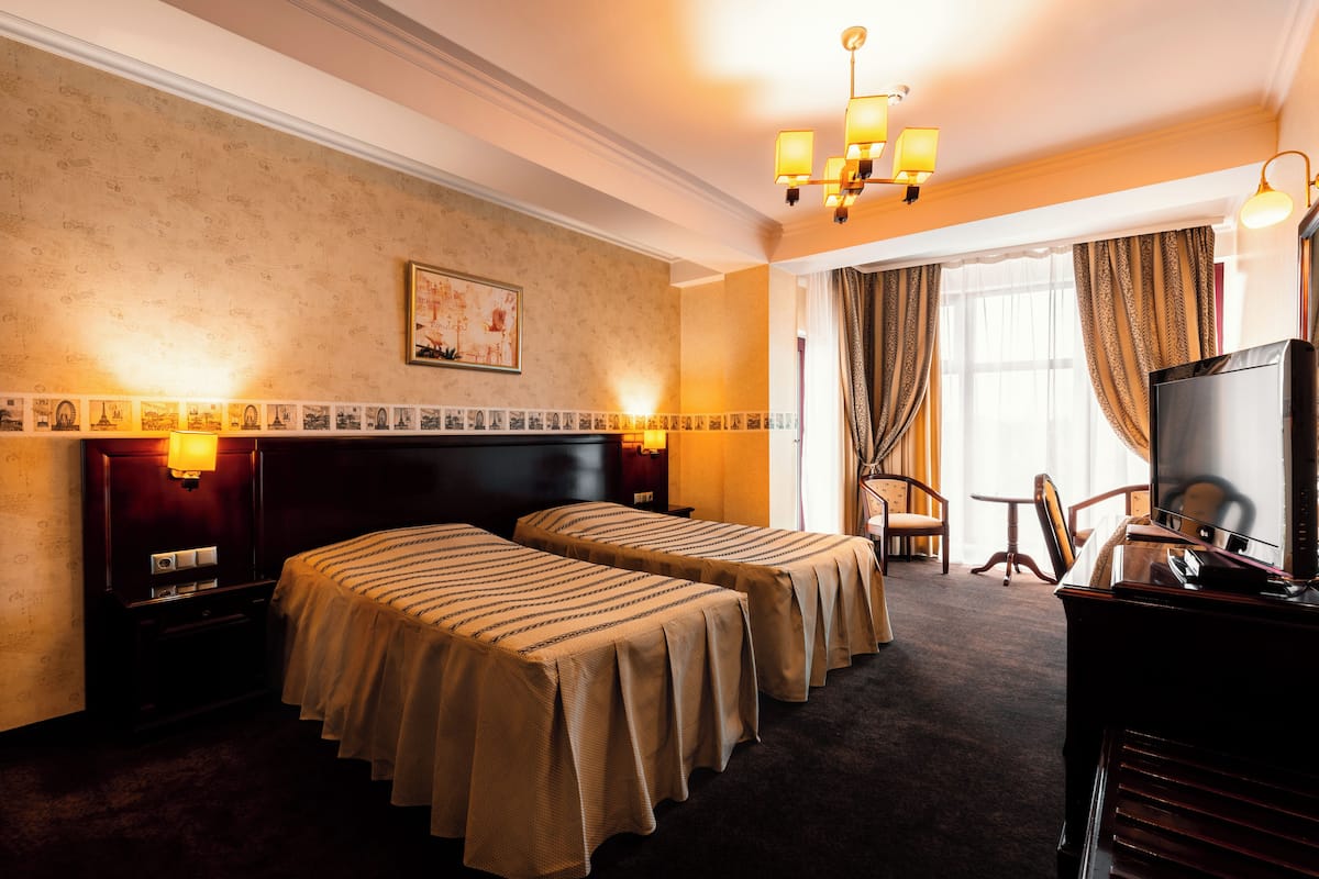 A hotel room with two beds, a desk, a TV, and a chair.