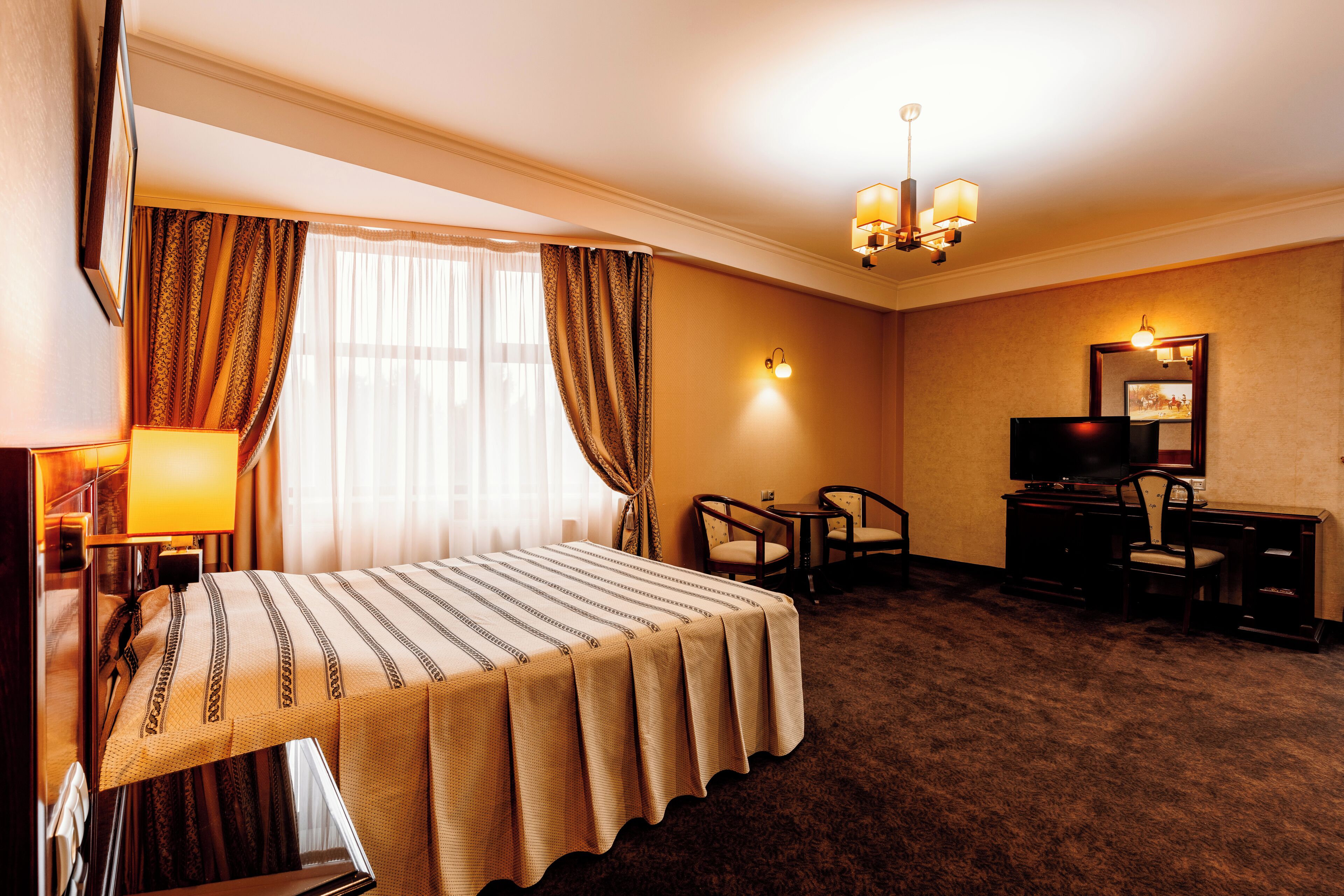 Una habitación de hotel con cama, escritorio, dos sillas, televisor y lámpara.
