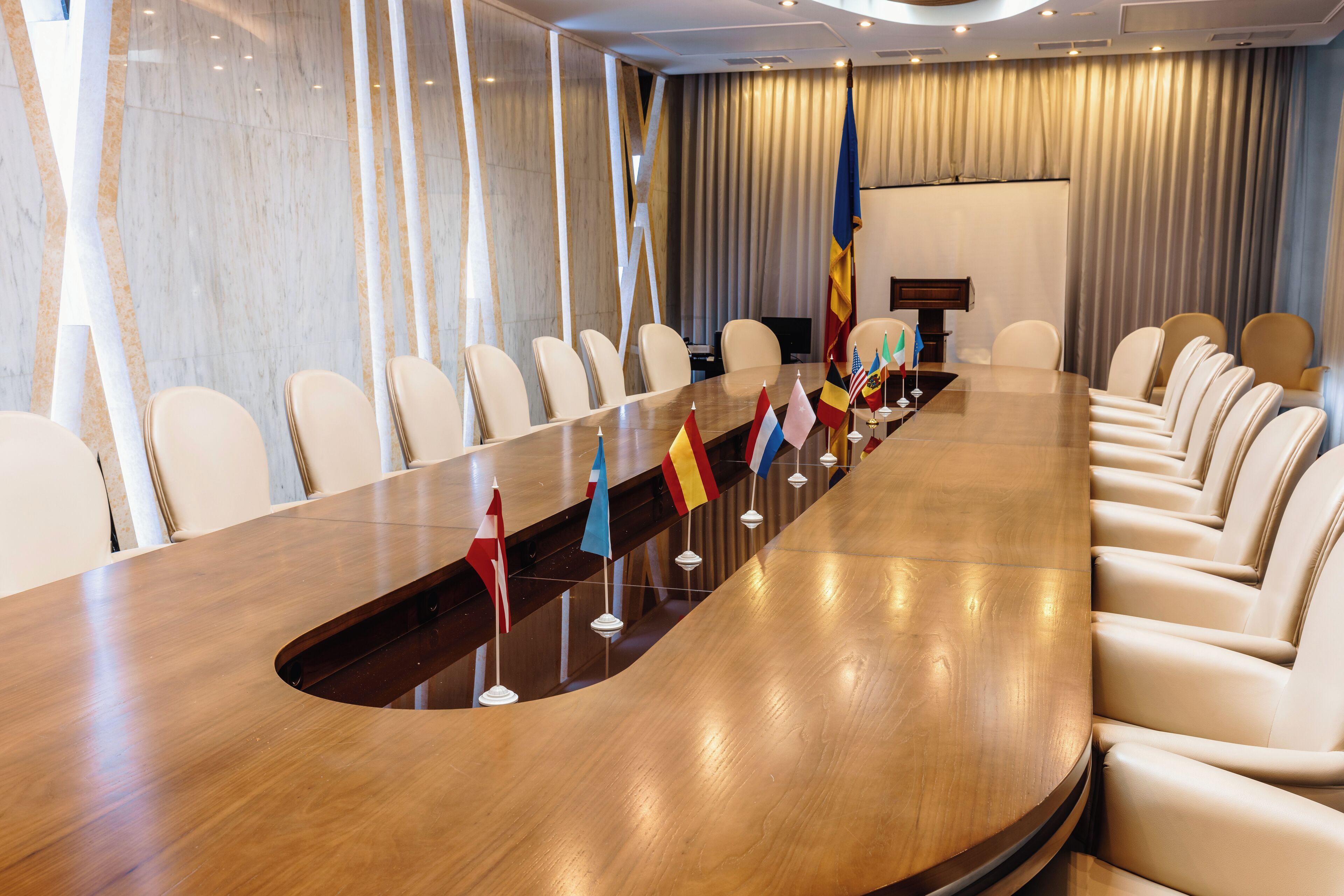 A conference room with a long table, multiple flags, and leather chairs.