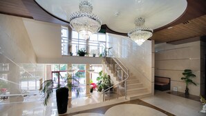A spacious lobby with a grand staircase, large chandeliers, and potted plants. - President Hotel (Bacioi)