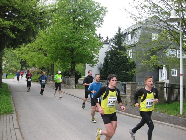 A group of runners on a paved path with trees and houses in the background.
