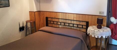 Une chambre à coucher avec une tête de lit en bois, une table de chevet avec une lampe, une chaise rouge et une petite table recouverte d’une nappe en dentelle.