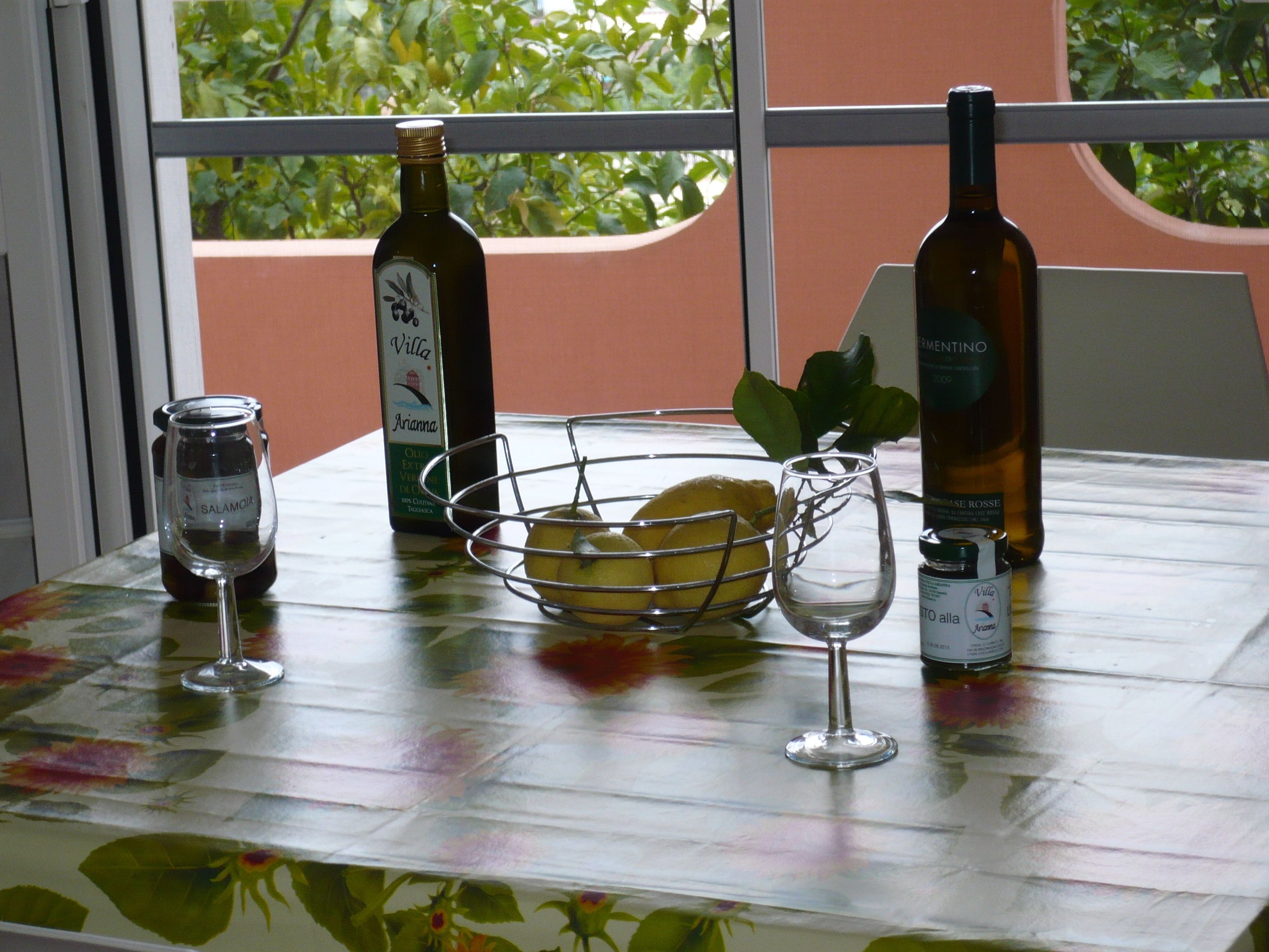 A table with a bottle of wine, a glass, a jar, and a metal basket containing a lemon.