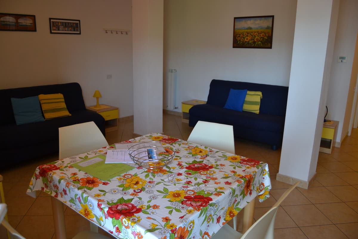 A living room with two sofas, a dining table with a floral tablecloth, and a painting on the wall.