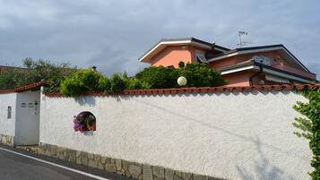 A white stucco wall with a stone base, a small window with a flower box, and a street in front.