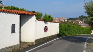 A white building with a red-tiled roof, a stone base, and a small window with purple flowers. - Azienda Agrituristica Villa Arianna (Imperia)
