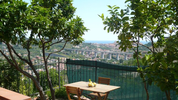 A terrace with a table and chairs, overlooking a cityscape with a bridge. - Azienda Agrituristica Villa Arianna (Imperia)