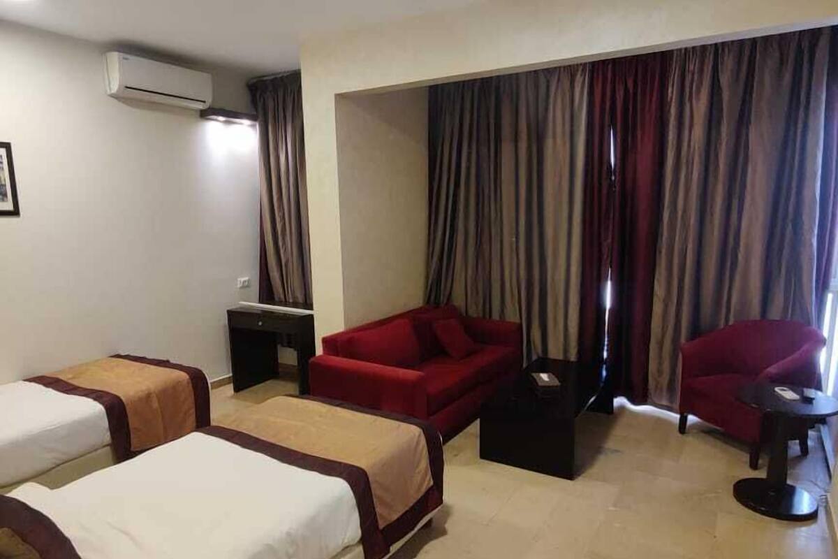 A hotel room with two beds, a red sofa, a small table, and a chair.