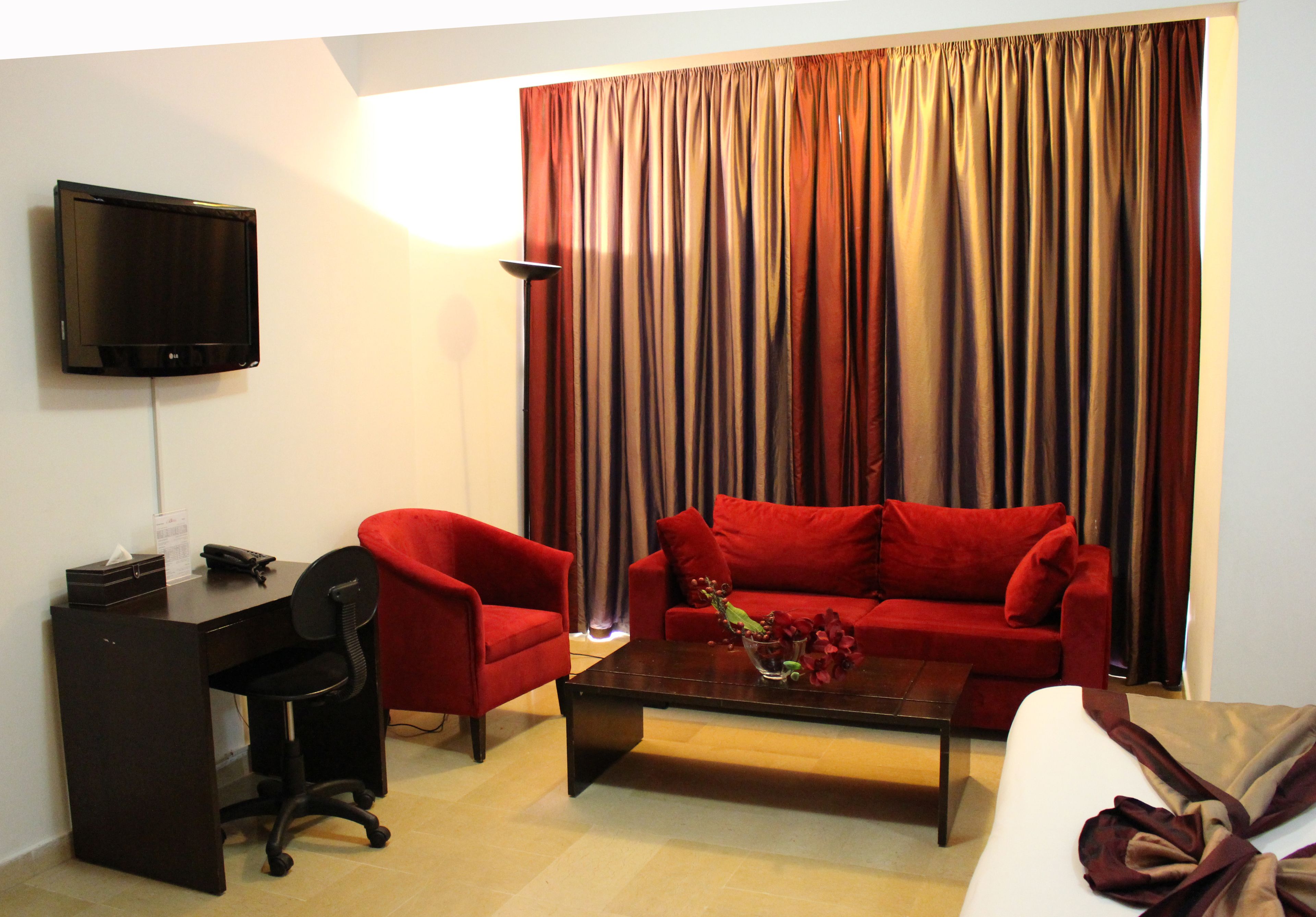 Una sala de estar con televisión, escritorio, dos sillones rojos, una mesa de centro y un sofá.