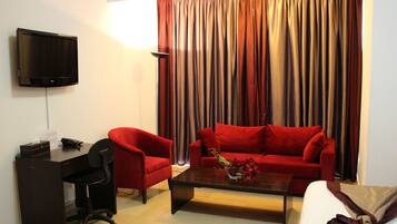 Una sala de estar con televisión, escritorio, dos sillones rojos, una mesa de centro y un sofá.