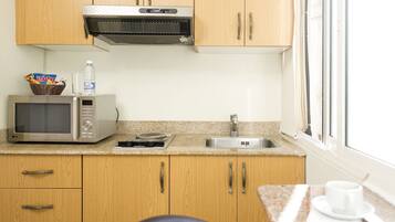 A compact kitchen with wooden cabinets, a microwave, a sink, and a window.