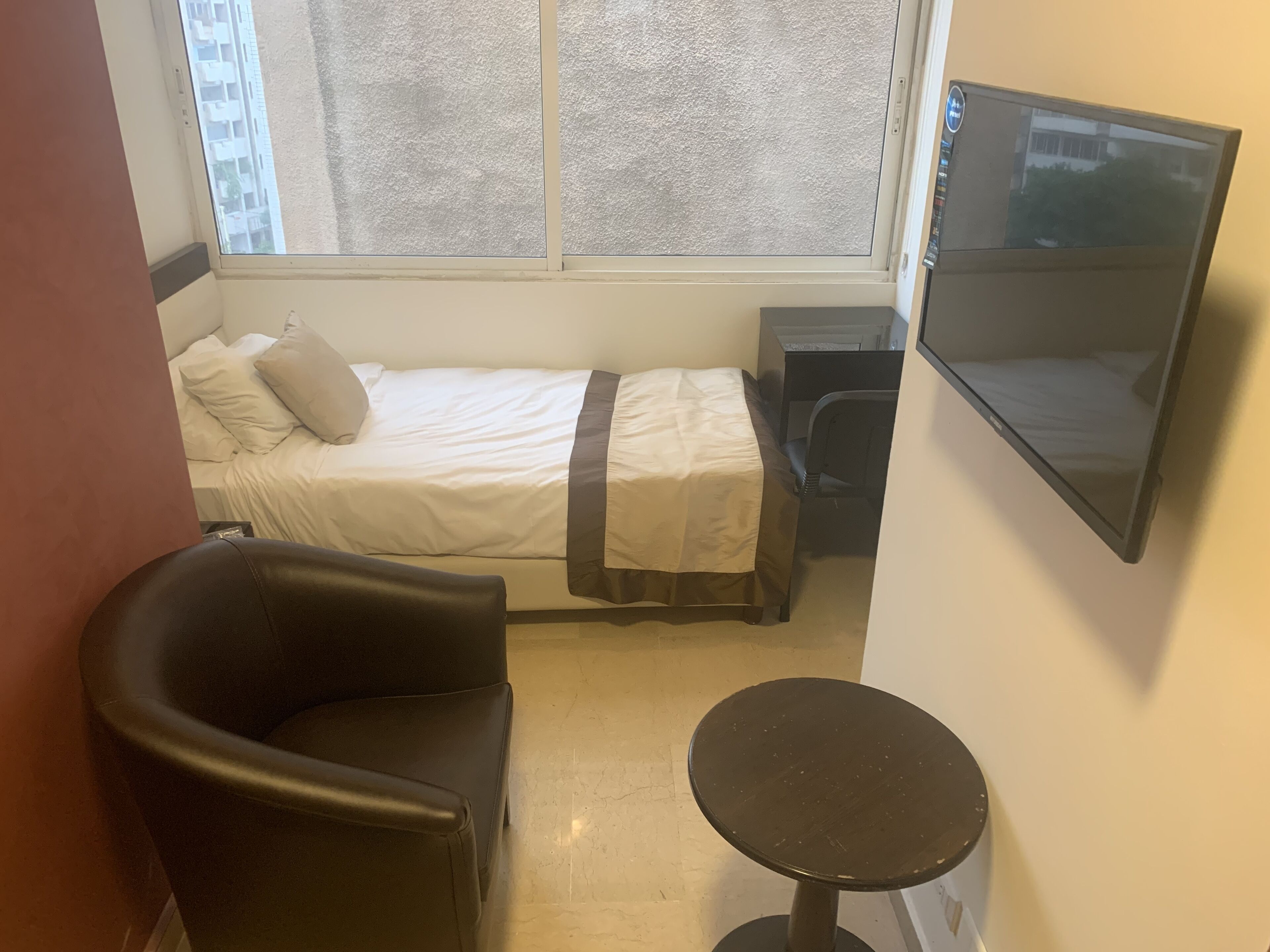 Une petite pièce, de taille modeste, comprenant un lit, un bureau, une chaise et un téléviseur.