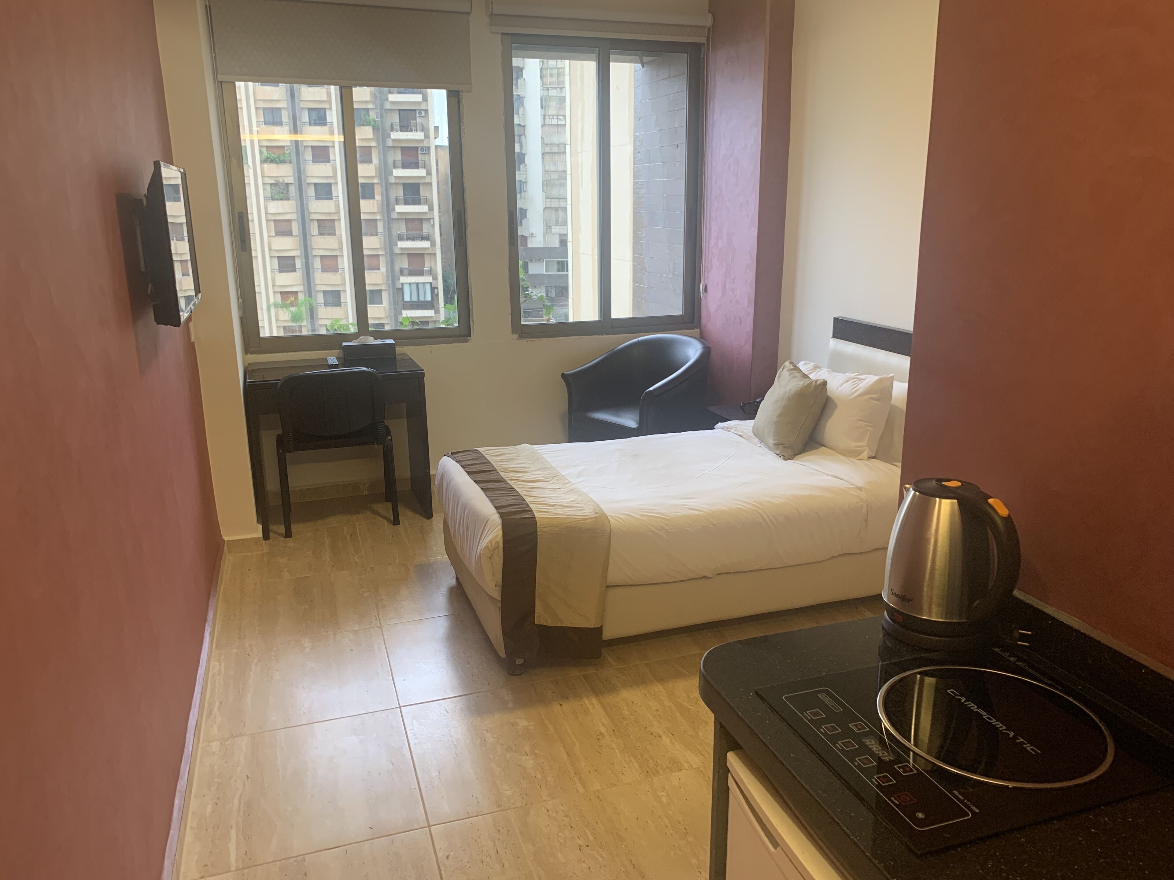 A hotel room with a bed, a desk, a chair, a window, and a coffee maker.