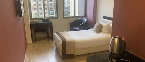 A hotel room with a bed, a desk, a chair, a window, and a coffee maker.