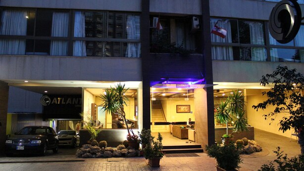 A hotel entrance with a reception desk, a staircase leading to the upper floors, and potted plants around the entrance. - Bliss 3000 Furnished Studios (Beirut)