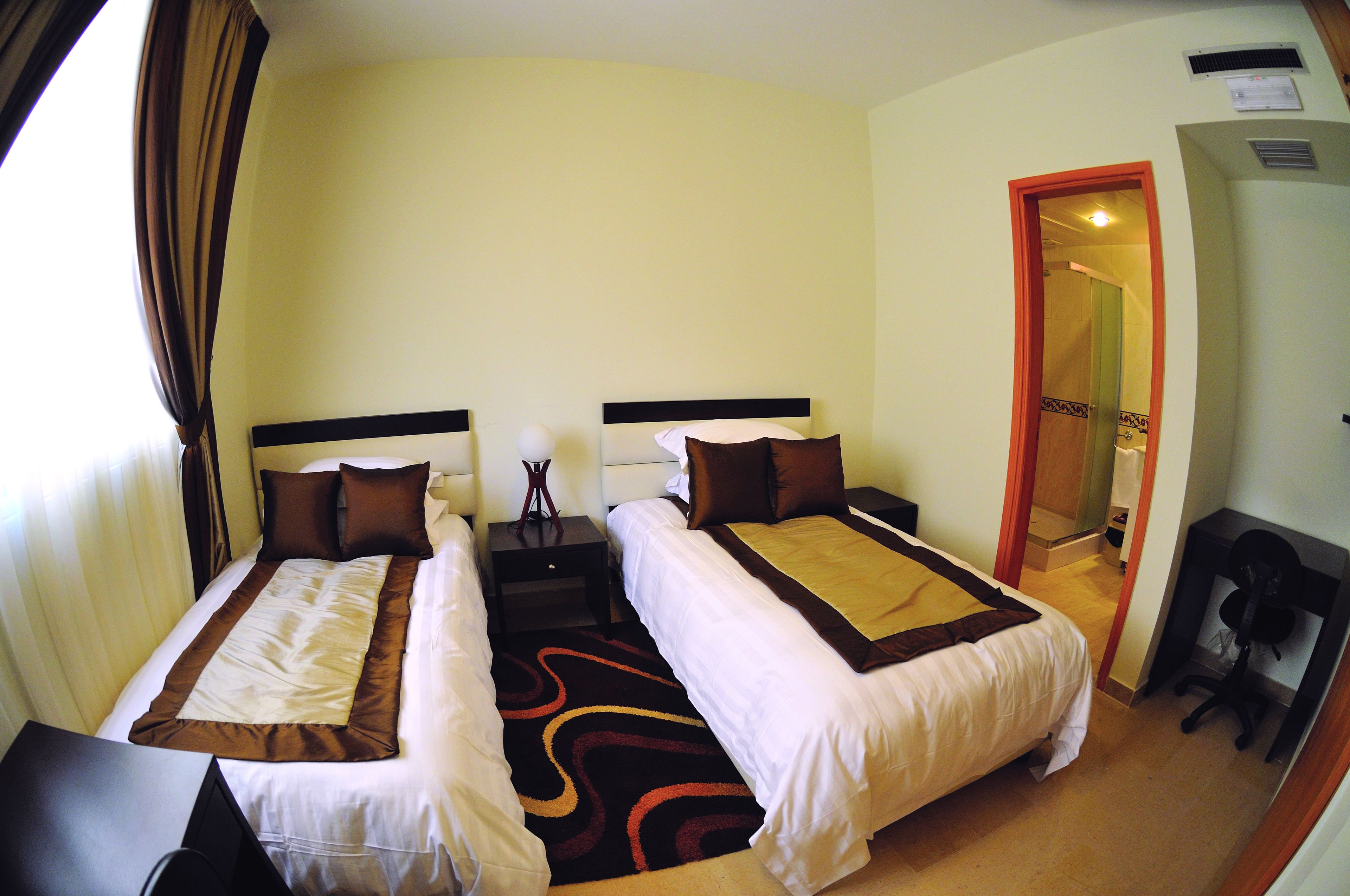 Une chambre d’hôtel avec deux lits, un bureau, une chaise et une salle de bain visible à travers une porte ouverte.