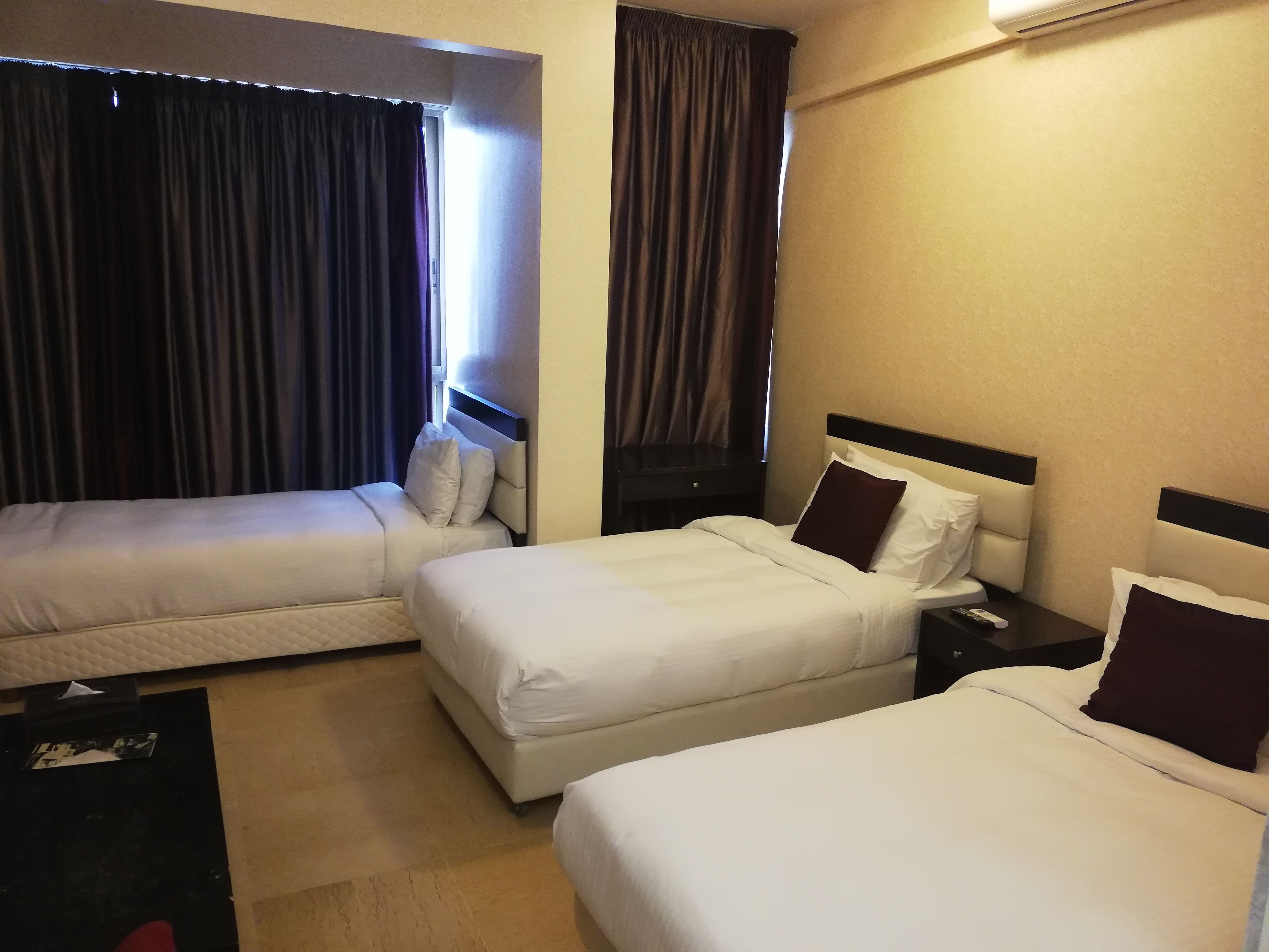 A hotel room with two beds, a nightstand, and a window with curtains.