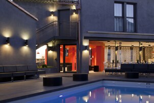Un área de piscina moderna con un edificio de dos pisos, asientos al aire libre y una zona de bar.
