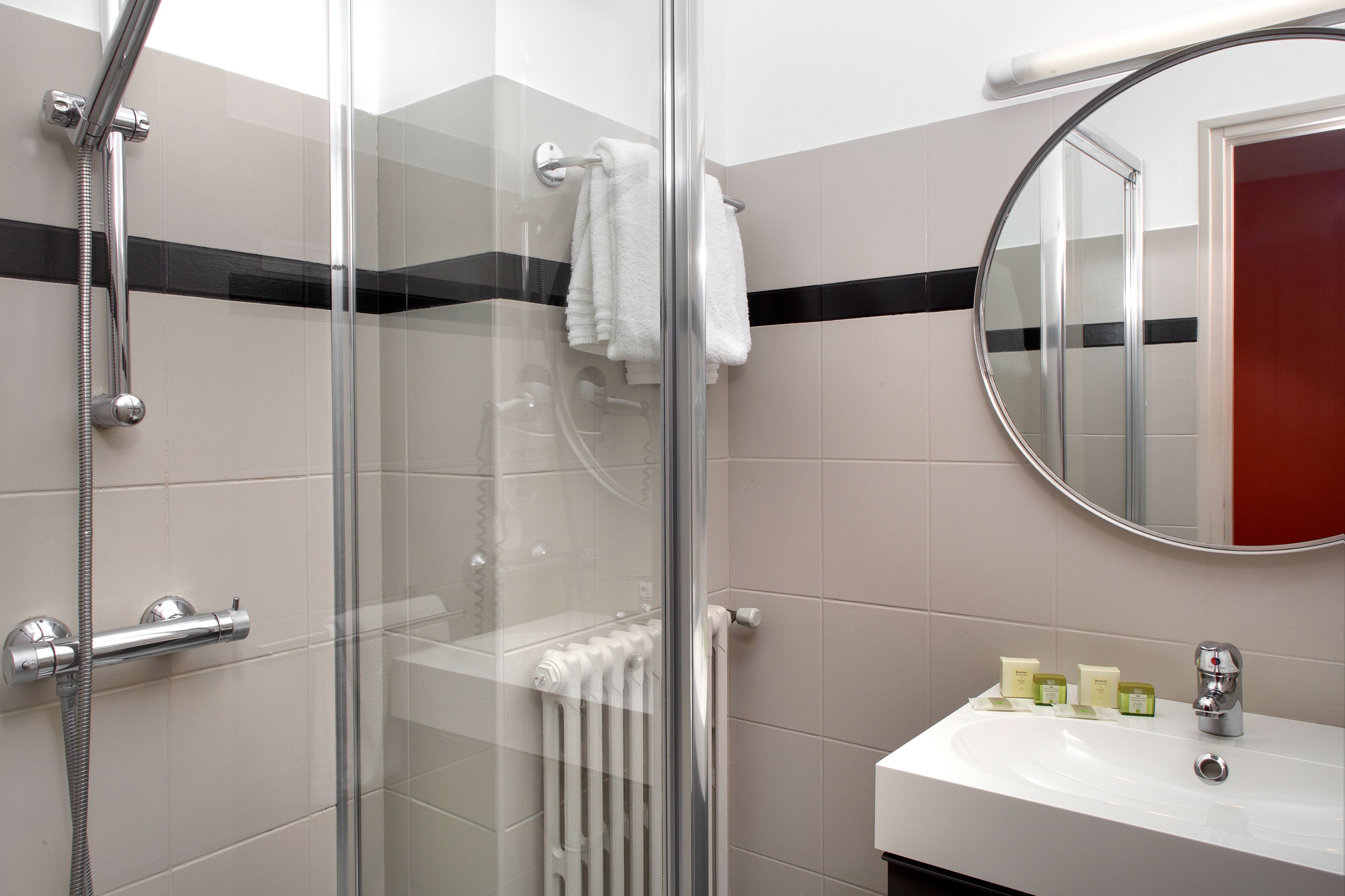 A bathroom with a glass shower enclosure, a white sink with toiletries, and a mirror.