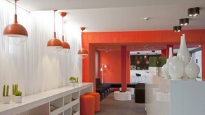 En modern inredning med en vit receptionsdisk, orange detaljer och hängande lampor.