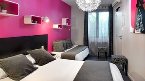 Ett modernt hotellrum med en rosa accentvägg, en stor säng med grå sängkläder, en taklampa och ett fönster med tunna, genomskinliga gardiner.