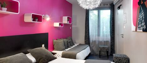 A modern hotel room with a pink accent wall, a large bed with grey bedding, a ceiling light fixture, and a window with sheer curtains.
