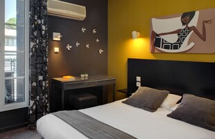 Habitación de hotel con cama, escritorio, silla, ventana con cortinas, aire acondicionado en la pared, reloj de pared y un cuadro.