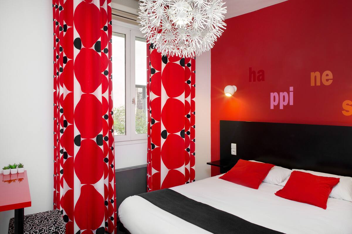 A modern bedroom with a red and white color scheme, a large bed with red pillows, a black headboard, and a decorative white chandelier.