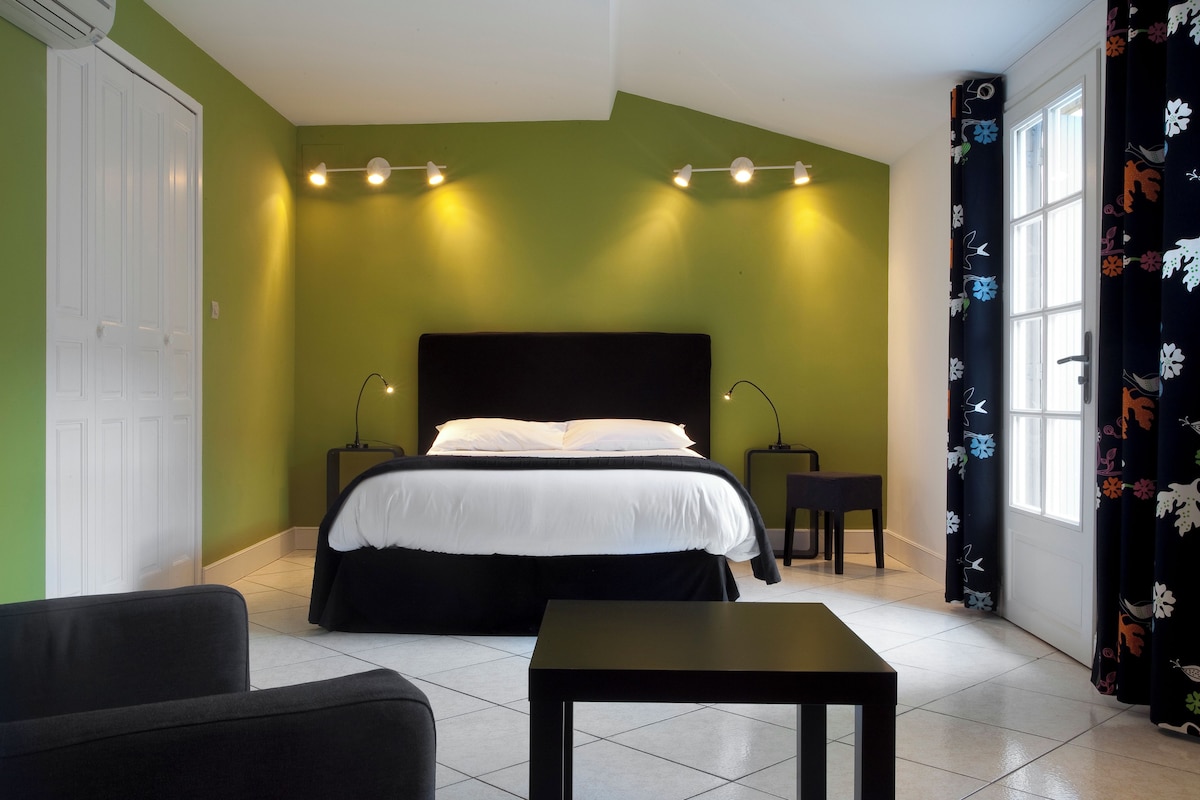 A hotel room with a large bed, two bedside tables, a small table, a chair, and a window with curtains.
