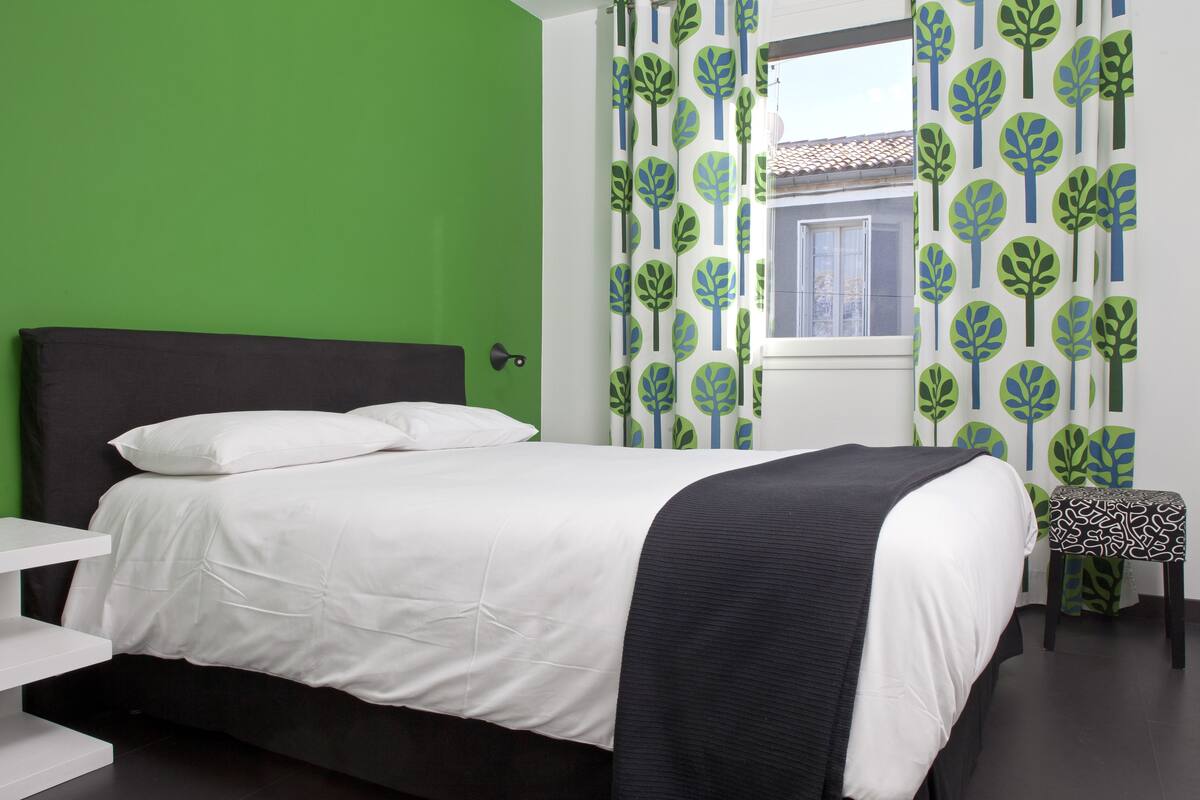 A bedroom with a bed, a bedside table, and a window with curtains.