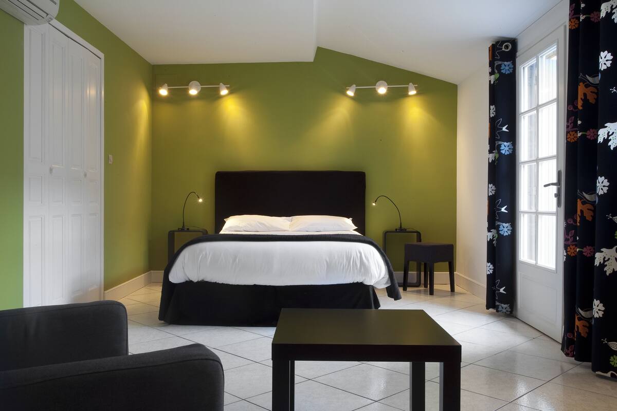 A bedroom with a bed, bedside tables, a chair, a table, and a window with curtains.