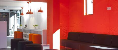 Un intérieur moderne avec un mur d’accent rouge, un canapé en cuir noir et des poufs orange.