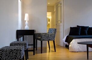 Una habitación con cama, una silla, una mesita y una lámpara.