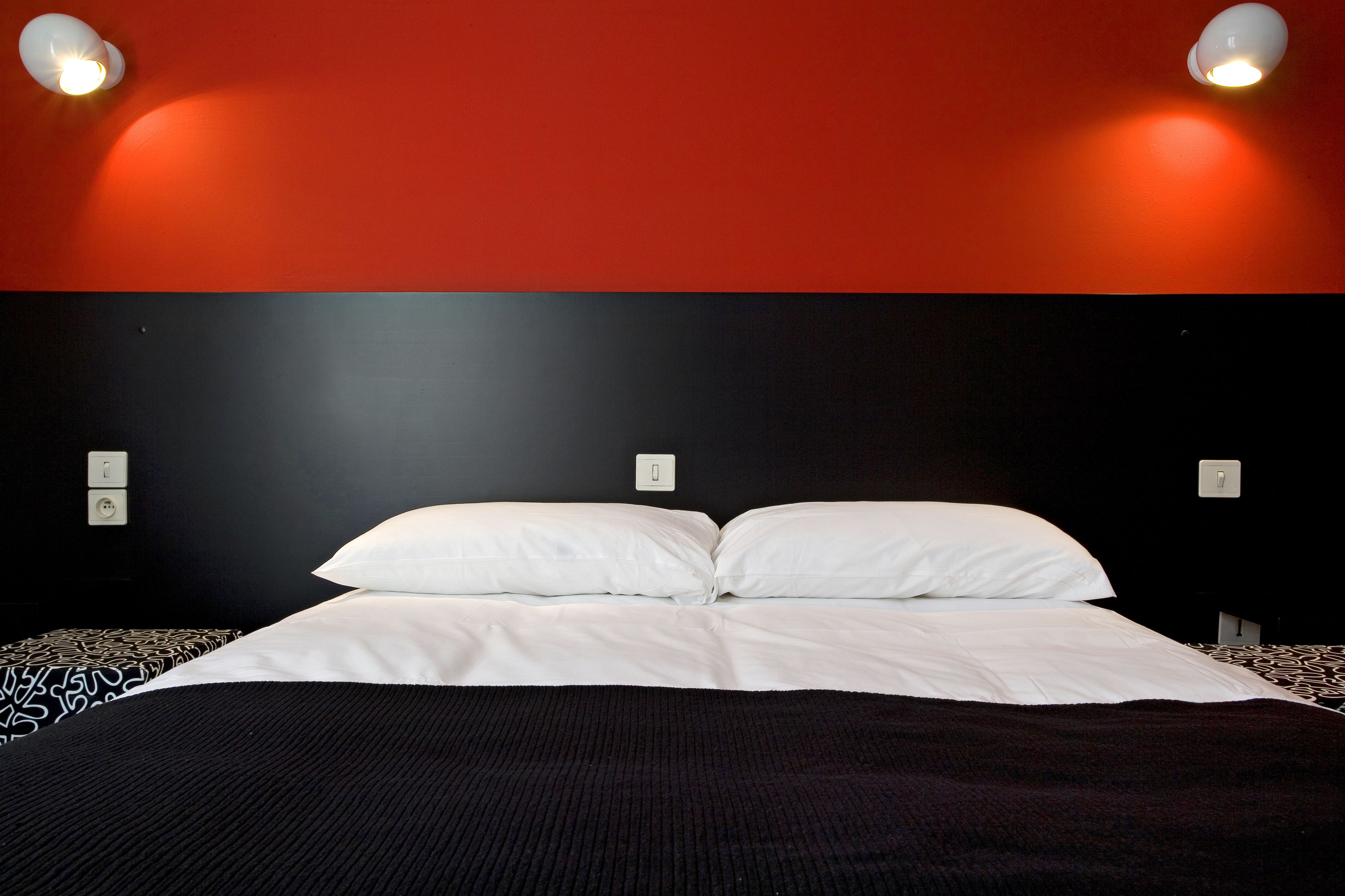 A hotel room with a large bed, two bedside lamps, and a red accent wall.