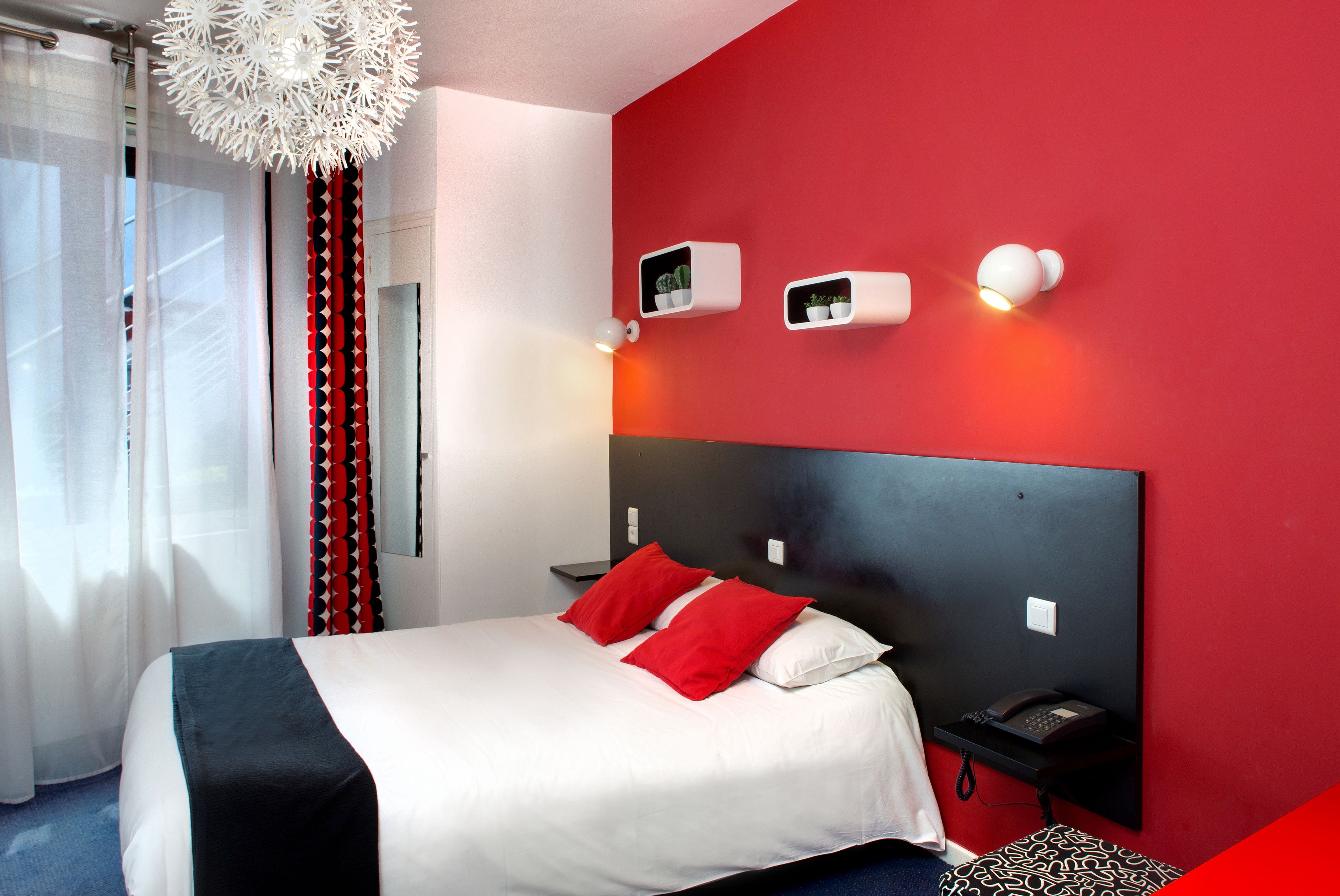 A modern hotel room with a large bed, red accent walls, and a white ceiling light fixture.