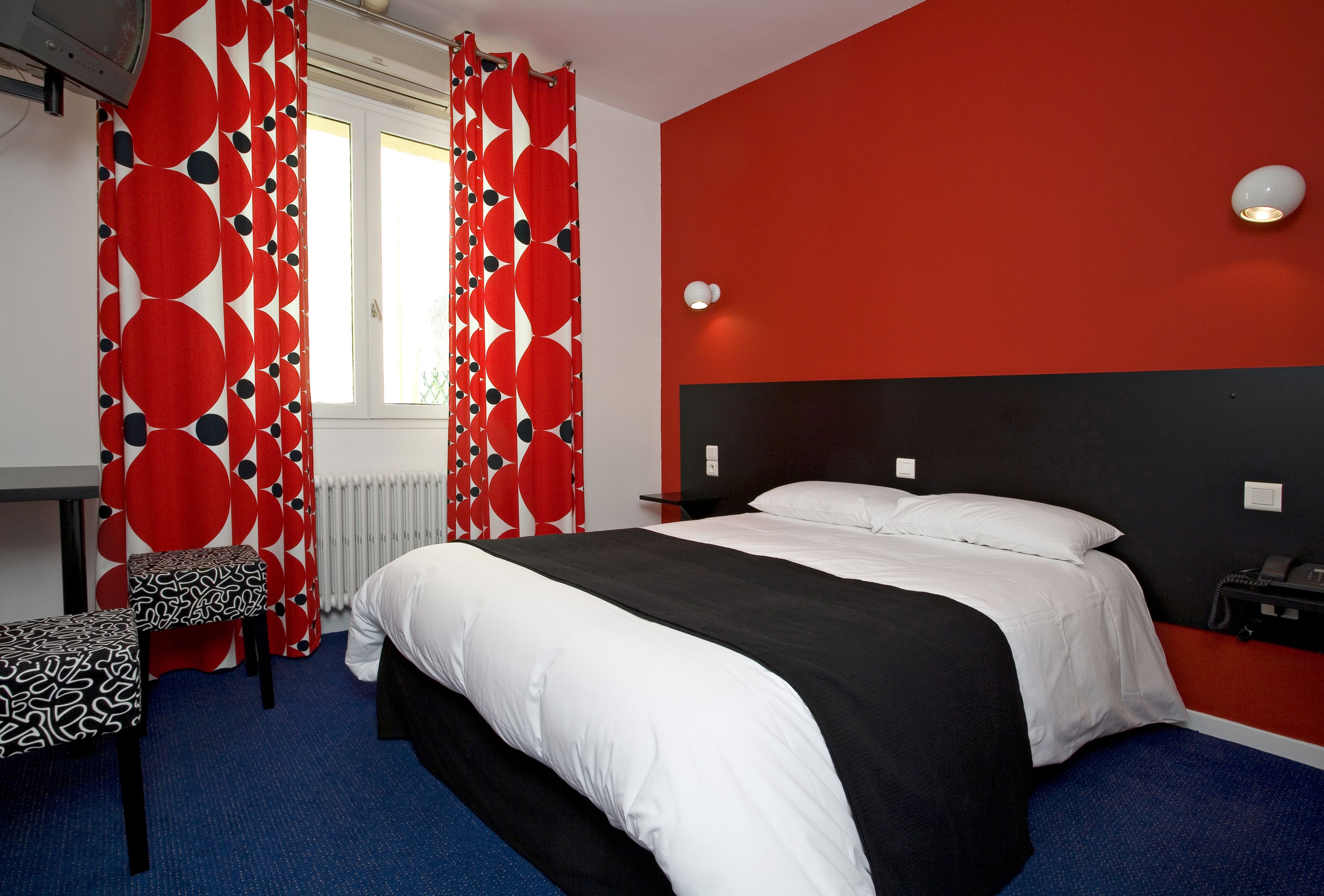 A hotel room with a bed, a chair, a desk, and a window with curtains.