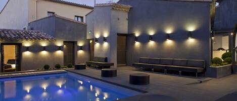 Zona de piscina exterior moderna con asientos e iluminación ambiental.