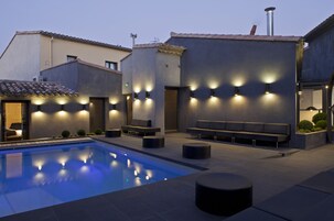 Zona de piscina exterior moderna con asientos e iluminación ambiental.