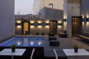 A modern outdoor pool area with seating and a small building with a tiled roof. - Hotel l'Octroi (Carcassonne)