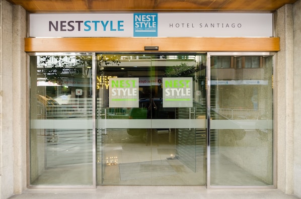 The entrance of Nest Style Hotel Santiago with clear signage and a modern glass facade.