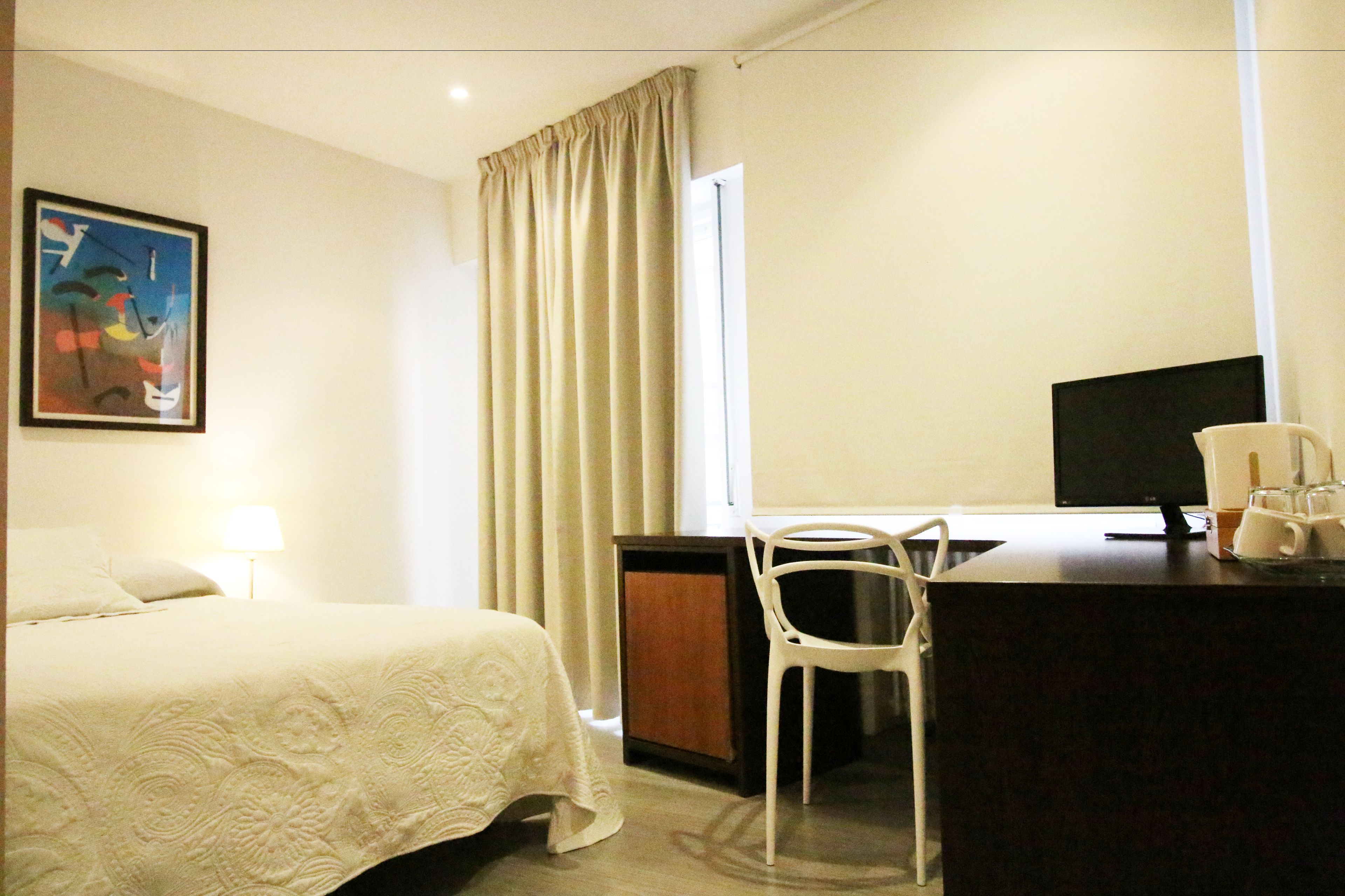 A hotel room with a bed, a desk with a chair, a television, and a window with curtains.